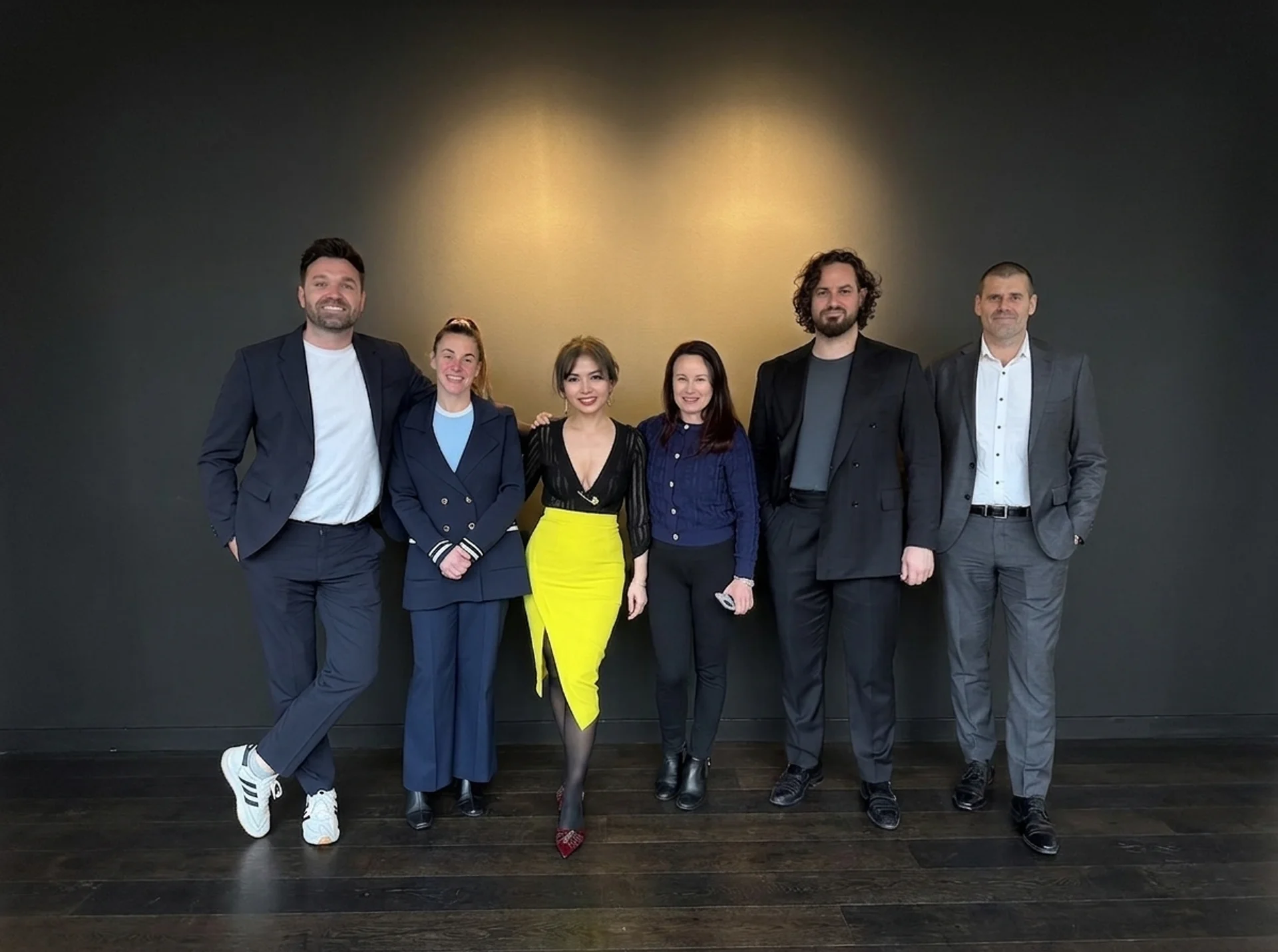 The six people of the OMD International team, standing together against a dark grey wall lit from behind.
